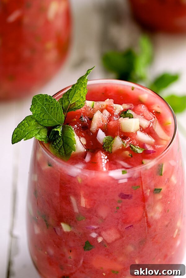 Close-up shot of refreshing Watermelon Gazpacho with Serrano Chiles and Mint in a glass, garnished with a sprig of fresh mint.