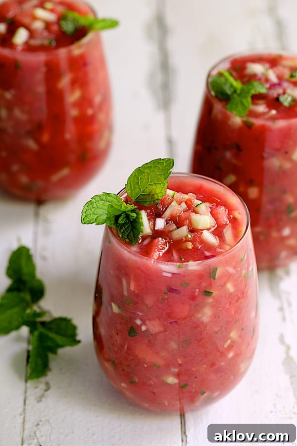 Three glasses of Watermelon Gazpacho with Serrano Chiles and Mint beautifully arranged on a white textured surface, showcasing its vibrant color and refreshing appeal.