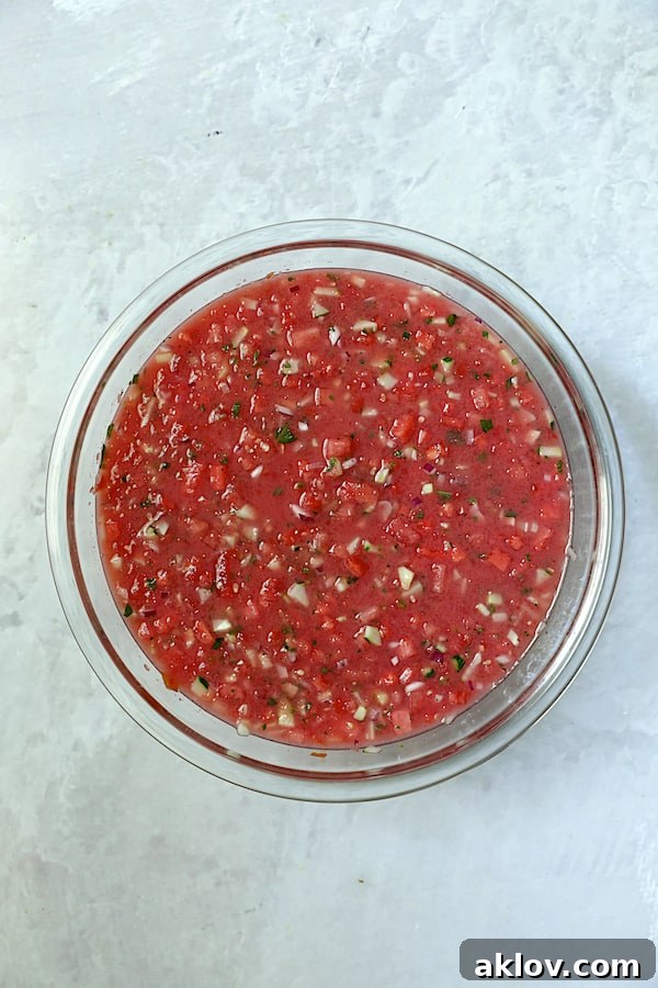 Watermelon Gazpacho, fully mixed with all ingredients, resting in a clear glass bowl, showcasing its rich texture and readiness for chilling.
