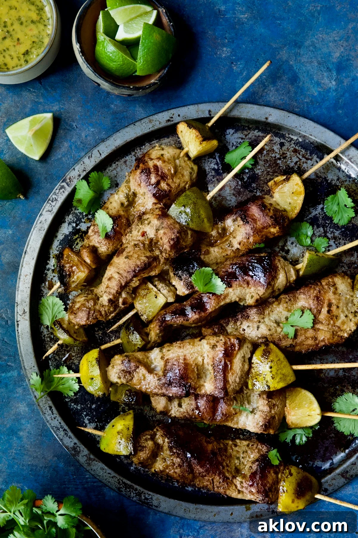 Grilled Mojo-Marinated Pork Skewers on a metal tray, garnished with fresh cilantro and lime wedges.