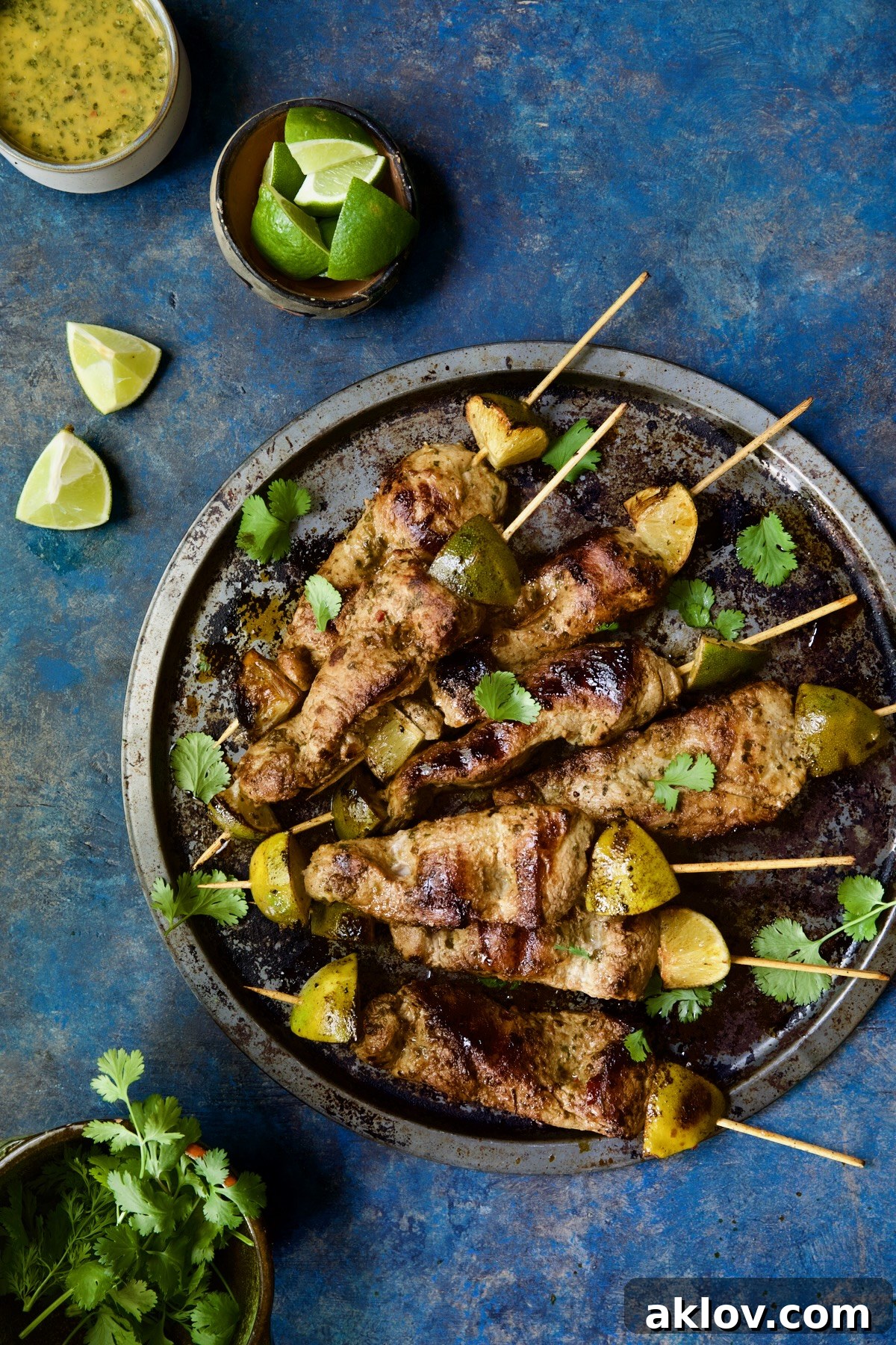 Platter of Mojo-Marinated Pork Skewers, accompanied by a bowl of dipping sauce, fresh lime wedges, and cilantro.