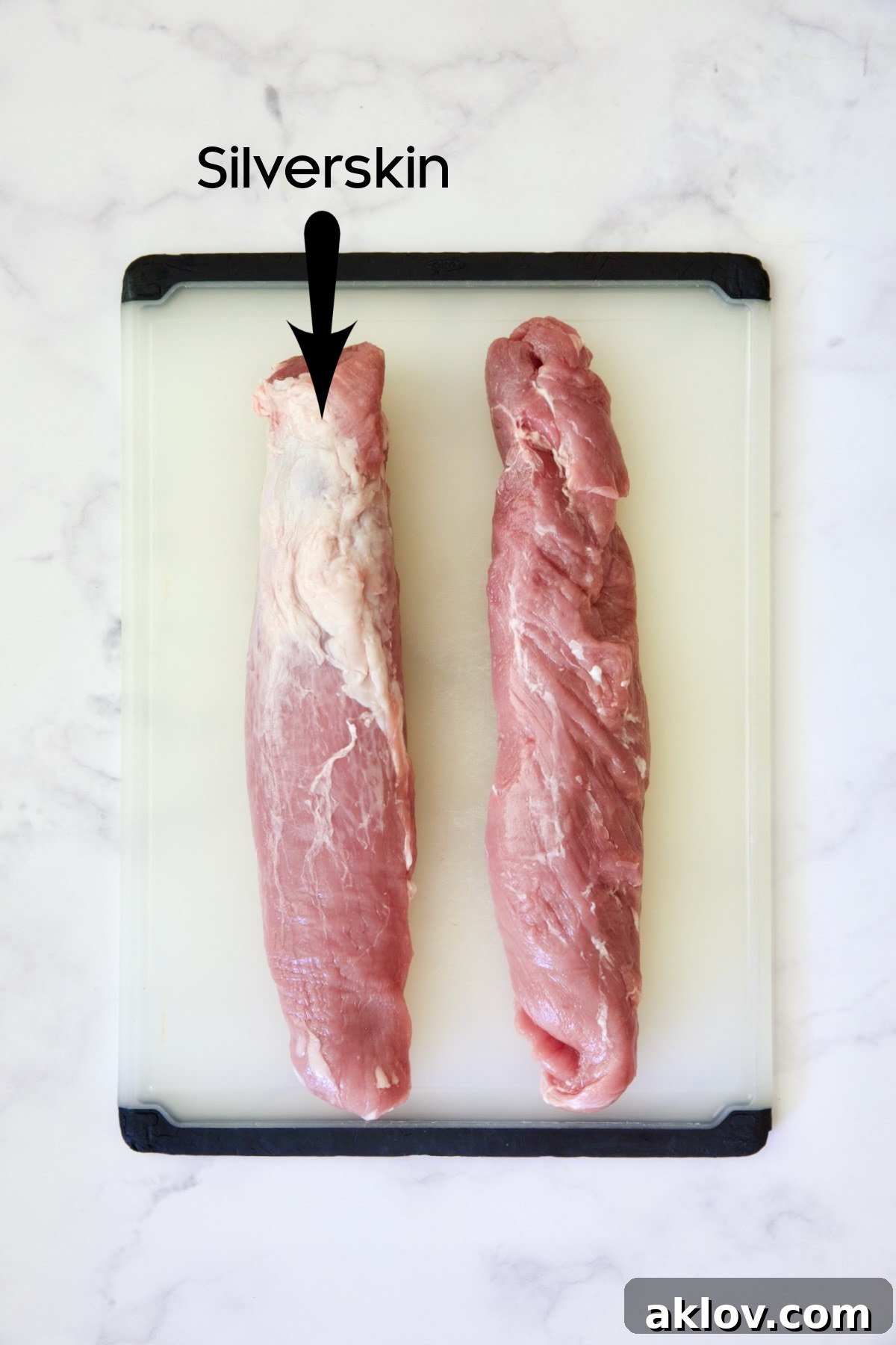 Two pork tenderloins on a white plastic cutting board, one untrimmed and the other ready for cutting.