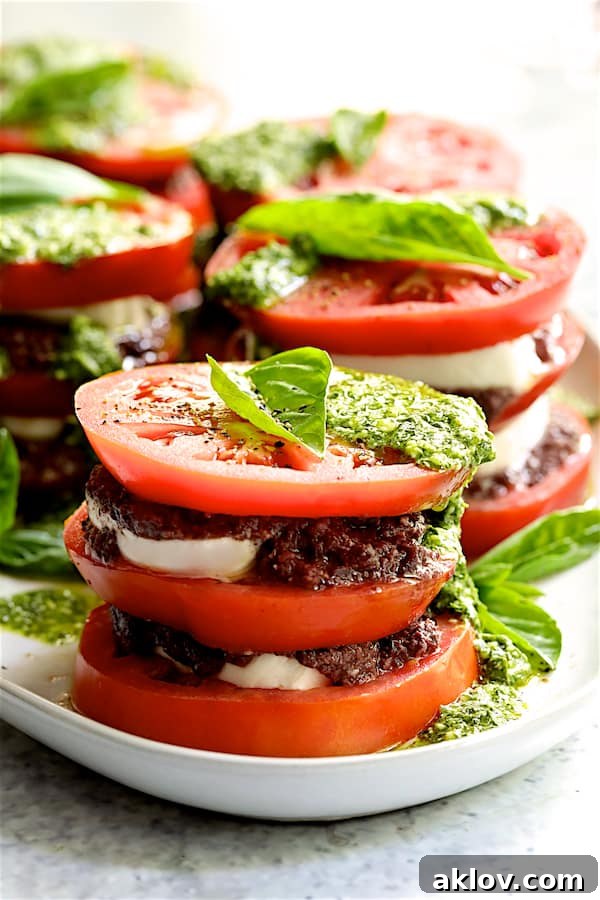 A wide shot of the exquisite Stacked Tomato Salad with Tapenade and Basil Pesto Dressing, artfully arranged on a pristine white platter, showcasing its vibrant colors and elegant presentation.