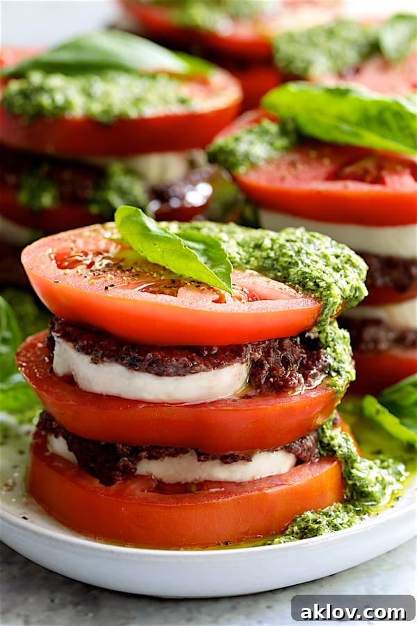 A close-up view of the Stacked Tomato Salad, richly drizzled with Basil Pesto Dressing and adorned with fresh basil leaves, highlighting the vibrant layers and appealing textures.