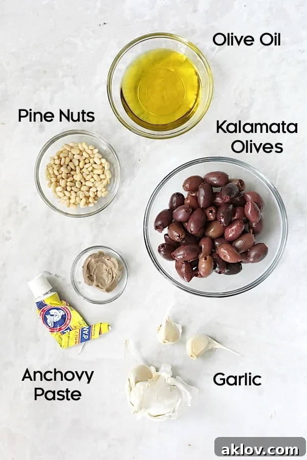 Close-up of tapenade ingredients—Kalamata olives, pine nuts, anchovy paste, and garlic—arranged in small glass bowls.