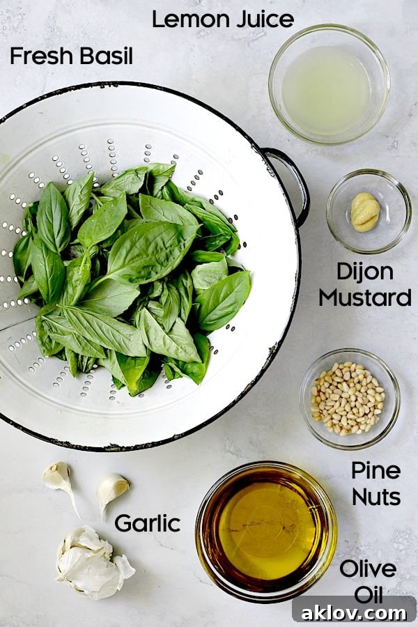 A collection of fresh ingredients for the basil pesto dressing: vibrant green basil leaves, bright yellow lemons, a jar of Dijon mustard, pine nuts, and garlic cloves.