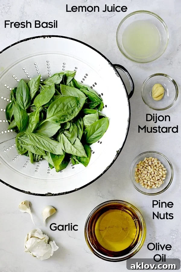Ingredients for basil pesto dressing, including fresh basil, pine nuts, lemon, garlic, and Dijon mustard, arranged for preparation.