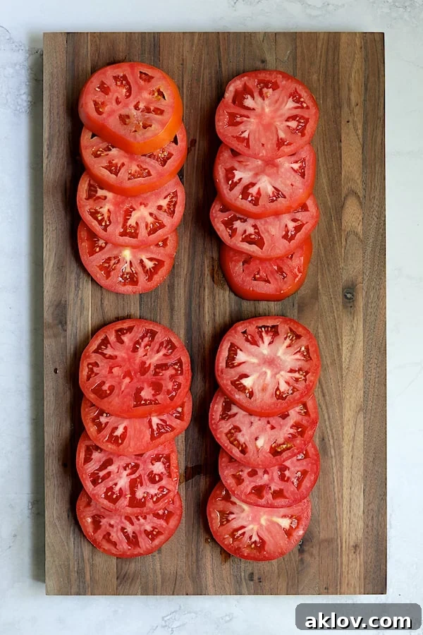 Sixteen perfectly sliced tomato pieces neatly arranged on a natural wood cutting board.