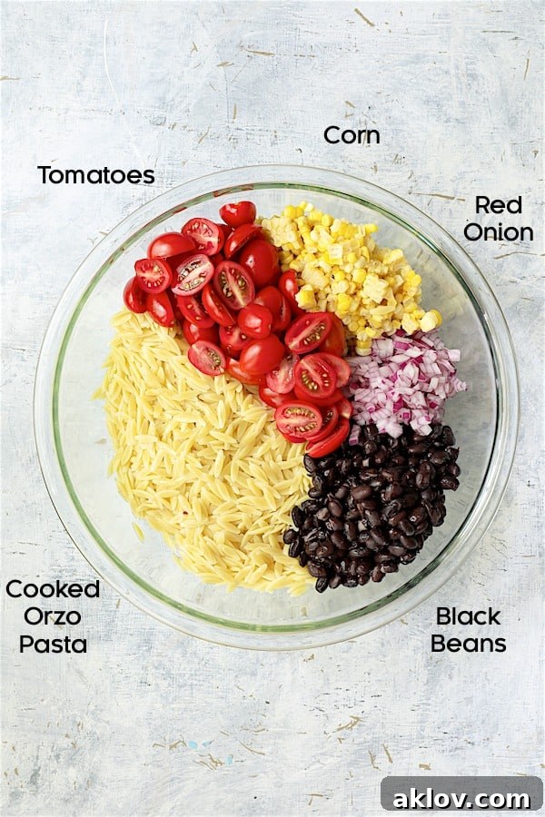 A glass bowl filled with the fresh, colorful ingredients for Southwestern Orzo Salad with Cilantro Lime Dressing, including tomatoes, corn, black beans, and red onion, awaiting the orzo and dressing.
