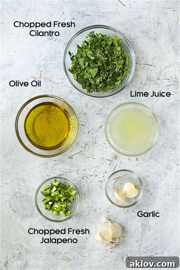 Assortment of fresh ingredients for the cilantro-lime salad dressing, including chopped cilantro, lime halves, jalapeño, and garlic cloves, presented in small glass bowls.
