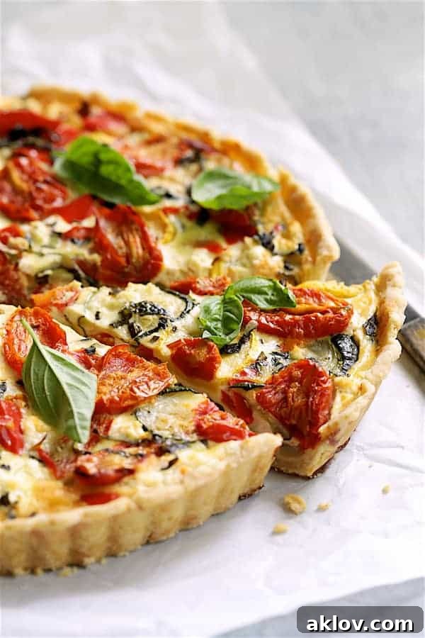 Photo of Provencal Vegetable and Goat Cheese Tart on white parchment paper with a slice cut from it.