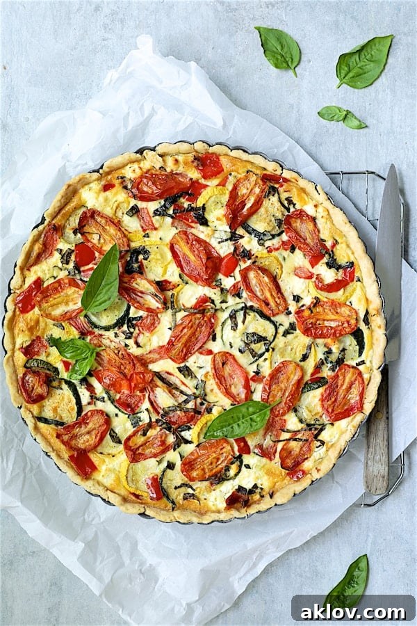 Photo of baked Provencal Vegetable and Goat Cheese Tart on parchment paper garnished with fresh basil.
