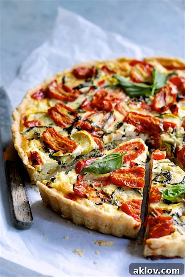 Photo of Provencal Vegetable and Goat Cheese Tart with tart slices on white parchment paper with knife.
