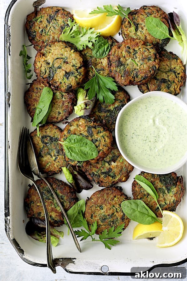 Crispy Zucchini Red Lentil and Spinach Fritters served with a side of creamy Cilantro Yogurt Sauce in a white pan, garnished with fresh herbs and lemon wedges.
