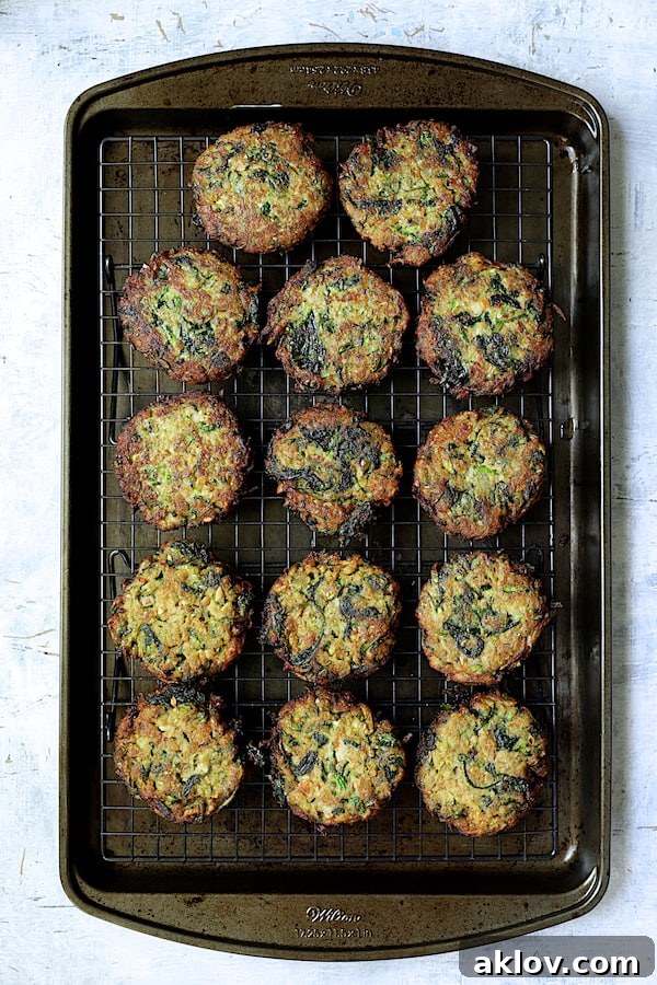 Freshly fried zucchini fritters cooling on a wire rack elevated over a baking sheet, ensuring optimal crispness.