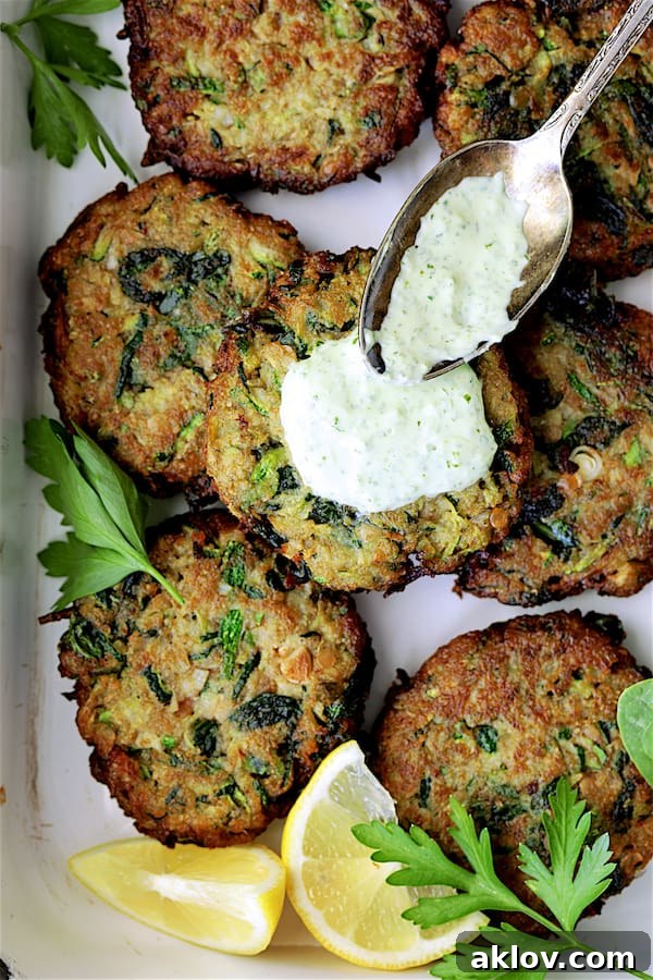 Cilantro Yogurt Sauce being generously drizzled over a plate of hot, crispy Zucchini Red Lentil and Spinach Fritters, highlighting their delicious pairing.