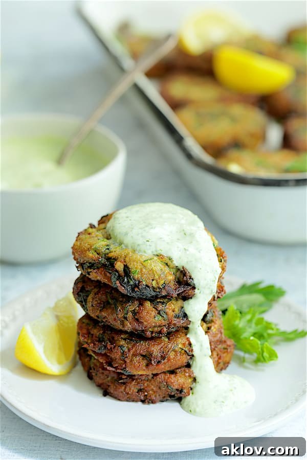 A visually appealing stack of four Zucchini Red Lentil and Spinach Fritters on a white plate, with creamy Cilantro Yogurt Sauce artfully dripping down the sides.