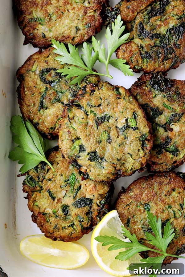 Close-up view of crispy Zucchini Red Lentil and Spinach Fritters, beautifully arranged with fresh green garnish and bright lemon wedges, ready to be served.