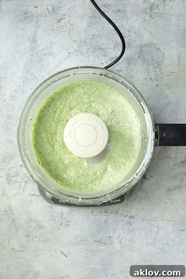 Vibrant green cilantro yogurt sauce being blended to a smooth consistency in a food processor, ready to complement the fritters.