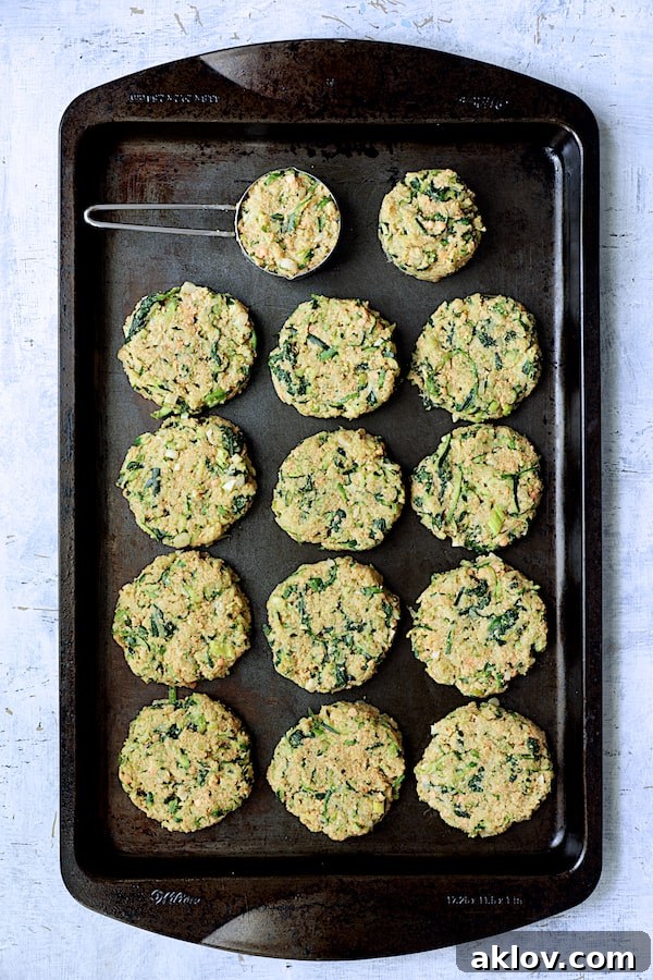 Several Zucchini, Red Lentil and Spinach Fritters sizzling in hot oil in a black baking sheet, cooking to a golden perfection.