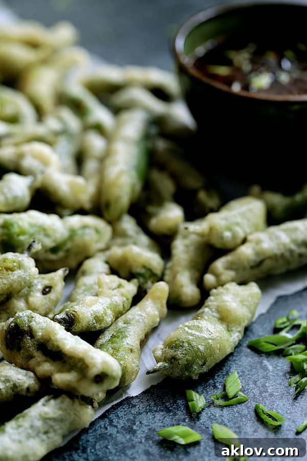 Close-up photo of Beer Batter Tempura Shishito Peppers with Spicy Garlic Dipping Sauce, highlighting the crispy texture and fresh garnish.