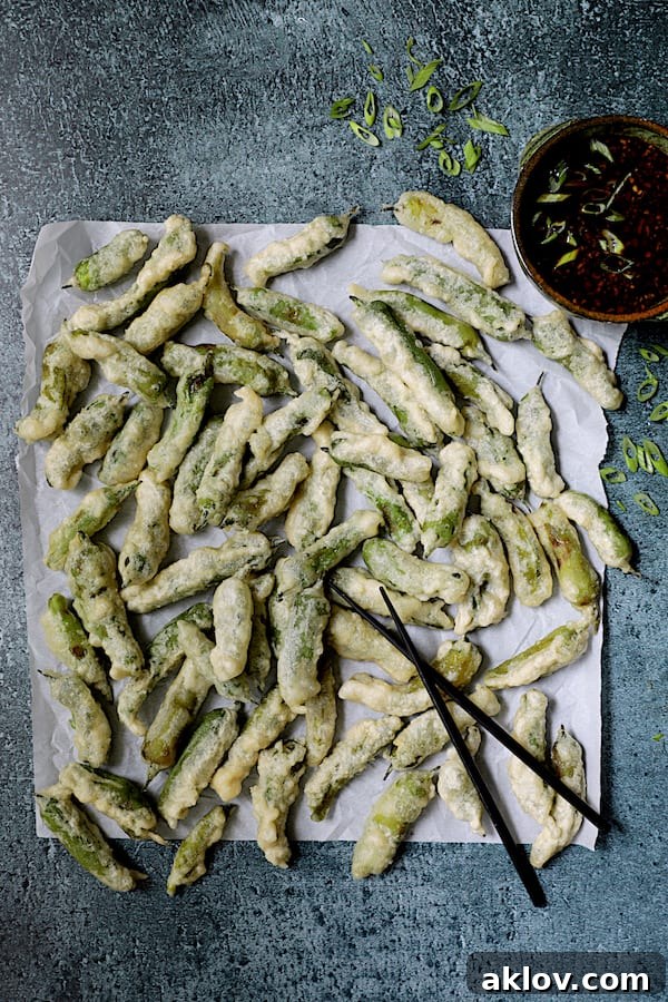 Freshly made tempura shishito peppers on white parchment paper, ready to be served with black chopsticks.