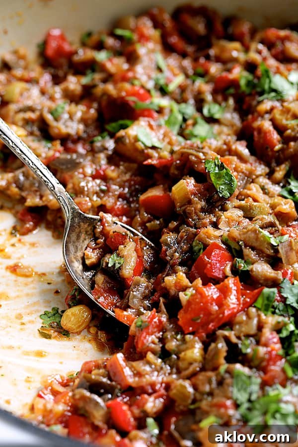 Close-up photo of finished Moroccan-Spiced Caponata in a white cast iron skillet with a serving spoon, ready to be enjoyed.