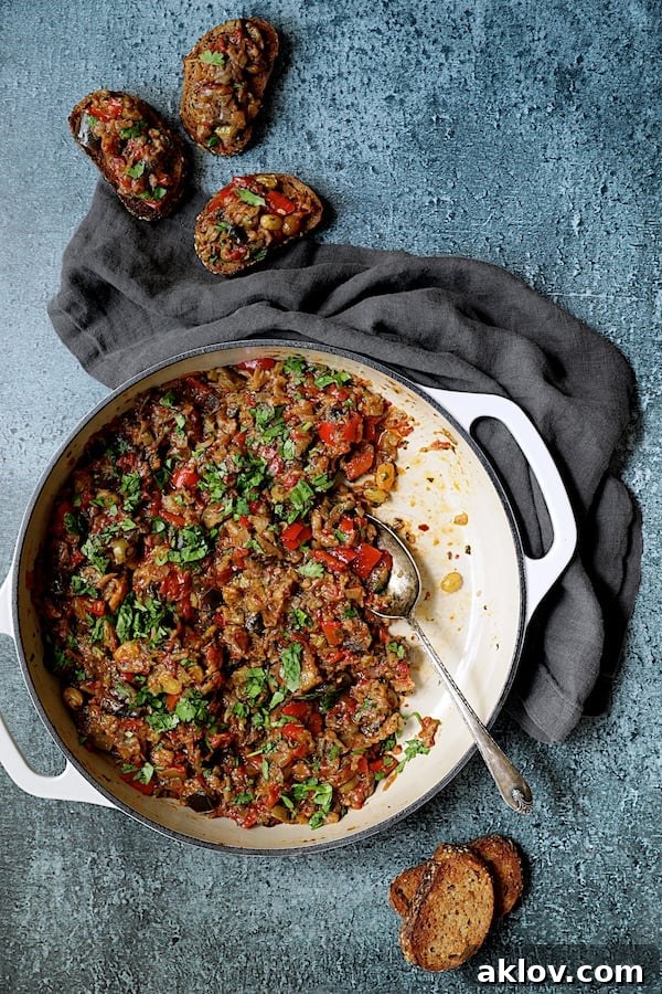 Photo of Moroccan-Spiced Caponata being served directly from a white cast iron skillet onto crusty bread.