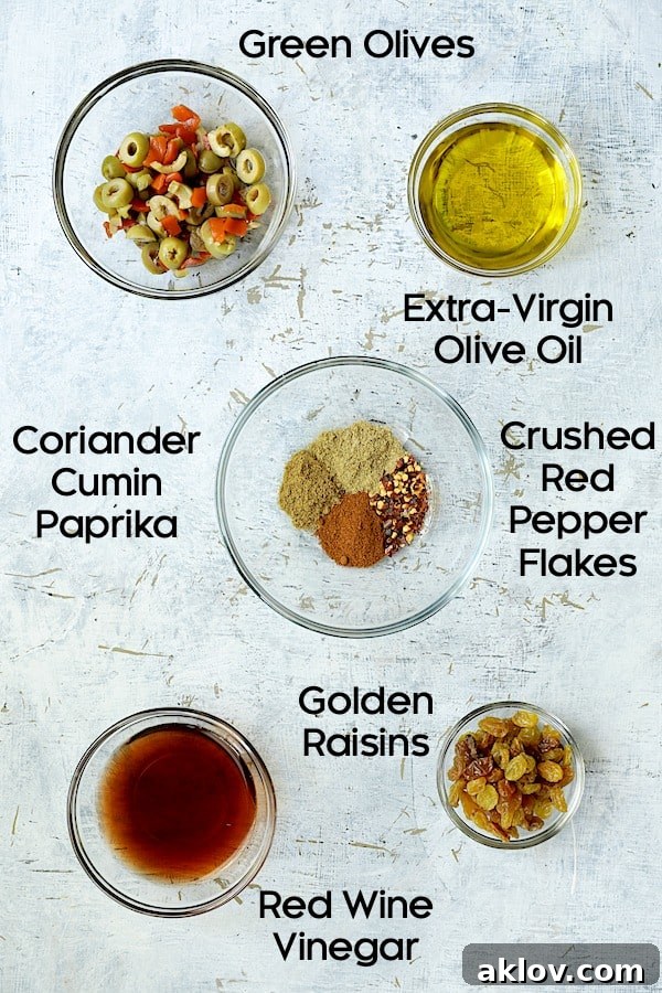 Photo of pantry ingredients for caponata, including olive oil, various spices, sliced green olives, golden raisins, and red wine vinegar in glass bowls.
