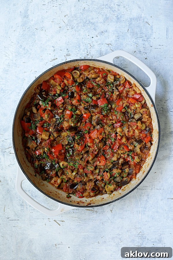Photo of finished caponata simmering in a white cast iron skillet, showcasing its rich, stewed appearance.