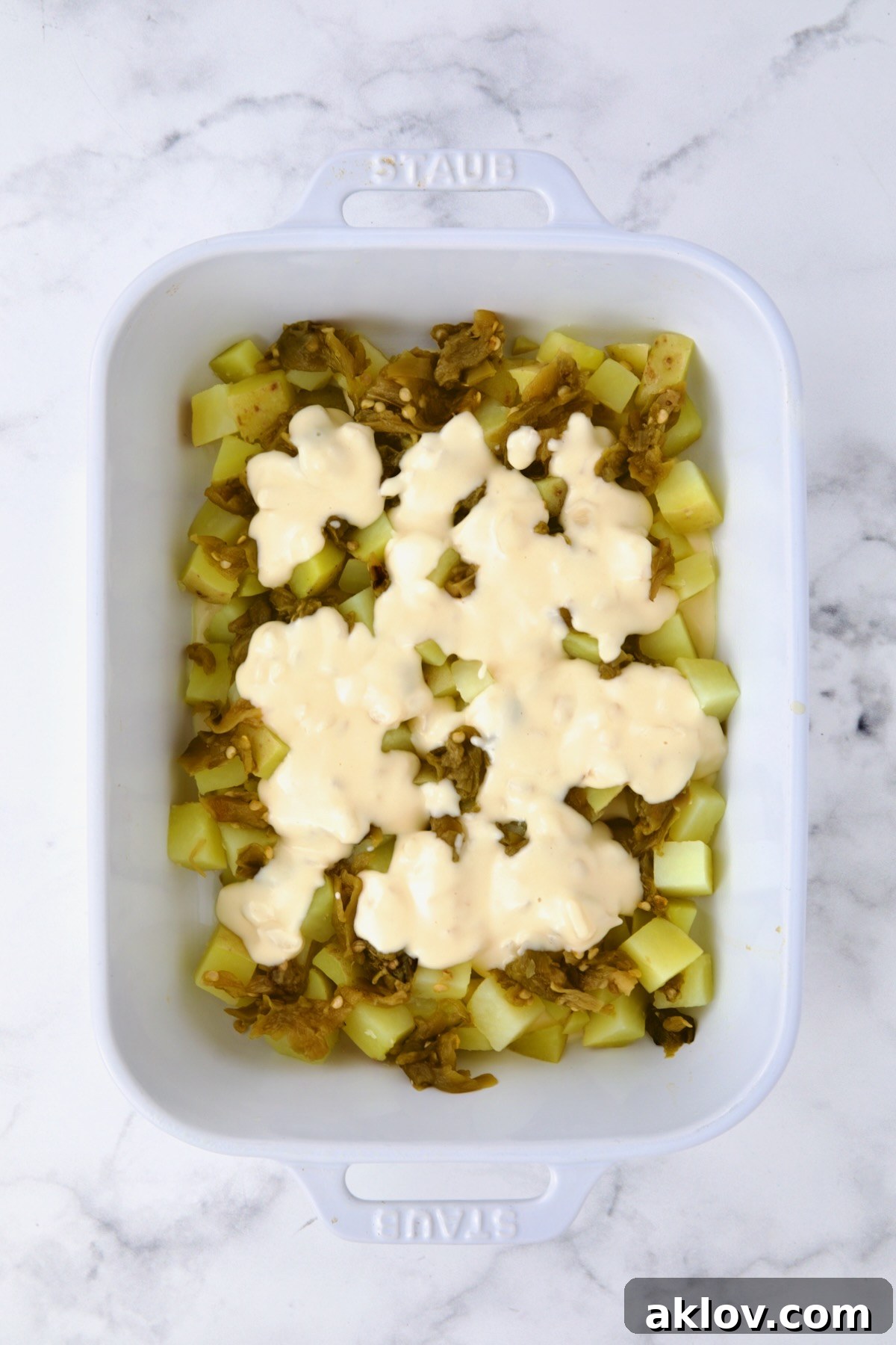 The first layer of potatoes and green chiles generously drizzled with the creamy, rich cheese sauce, ensuring every component is coated and ready for the next layer of assembly.