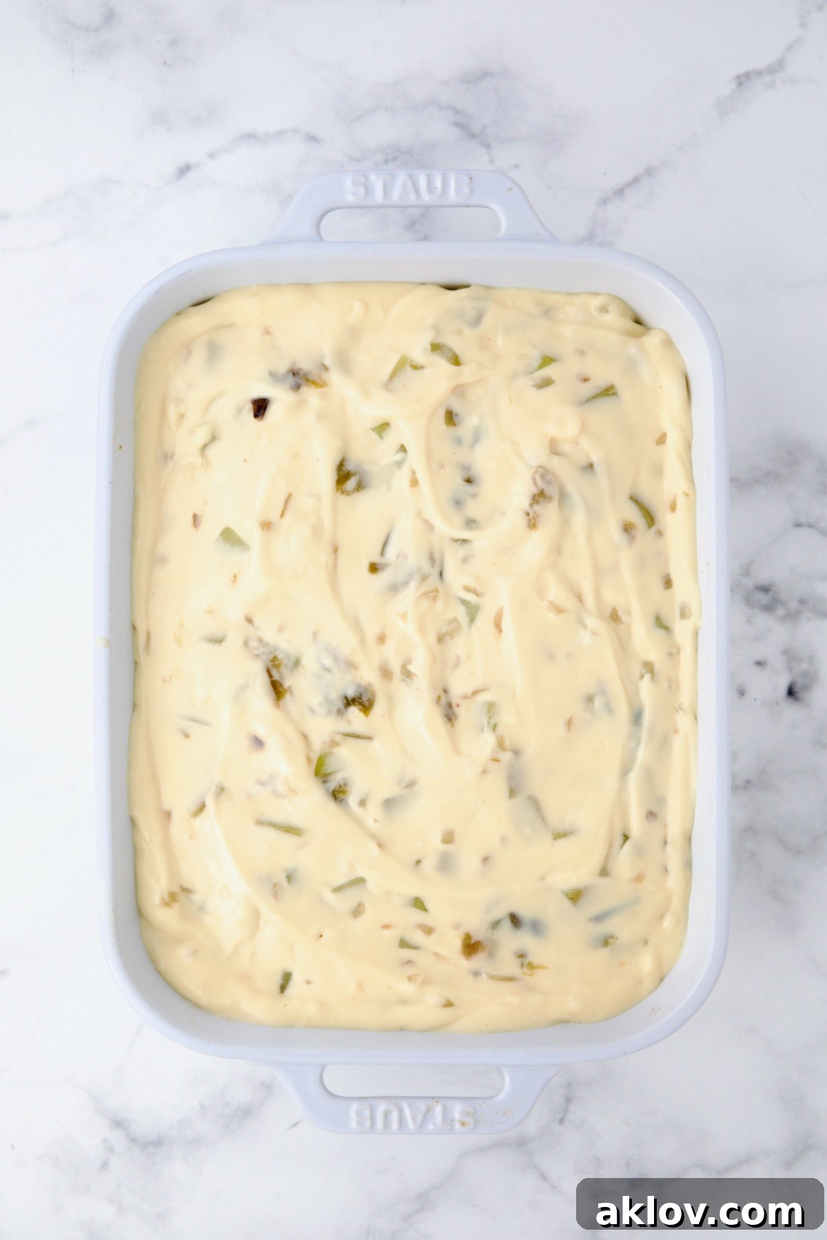 The fully assembled Hatch Green Chile au Gratin Potatoes in a white rectangular baking dish, with all layers of potatoes, green chiles, and cheese sauce neatly arranged and ready for baking. The top is generously covered with sauce.