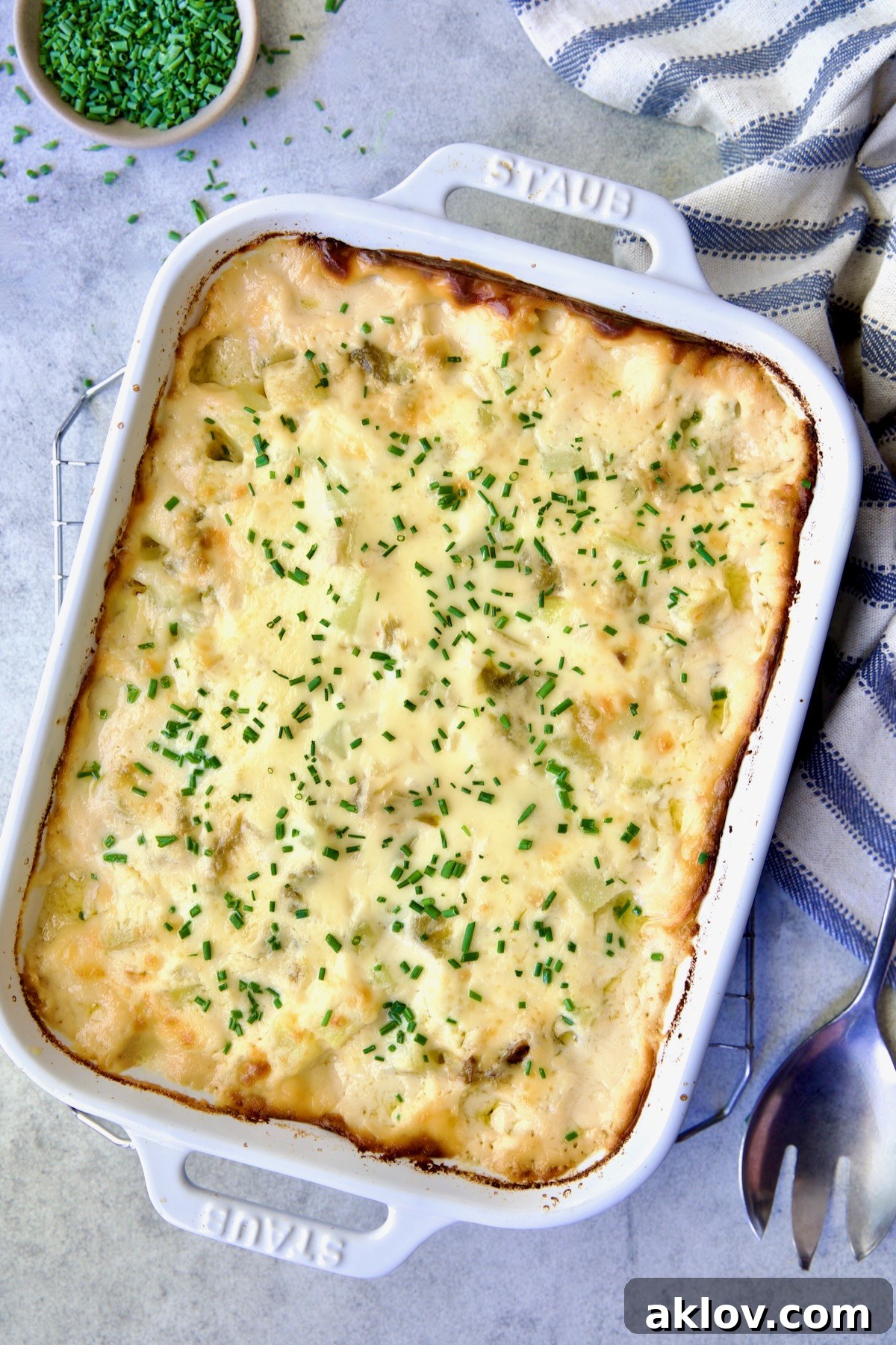 The beautifully baked Hatch Green Chile au Gratin Potatoes, fresh out of the oven, presenting a golden-brown, bubbly top in a pristine white rectangular baking dish. It’s ready to be served as a comforting and flavorful side.