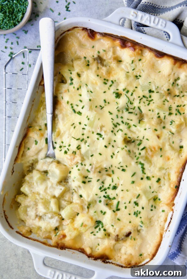 Hatch Green Chile au Gratin Potatoes in white rectangular baking dish with serving spoon scooping some out.