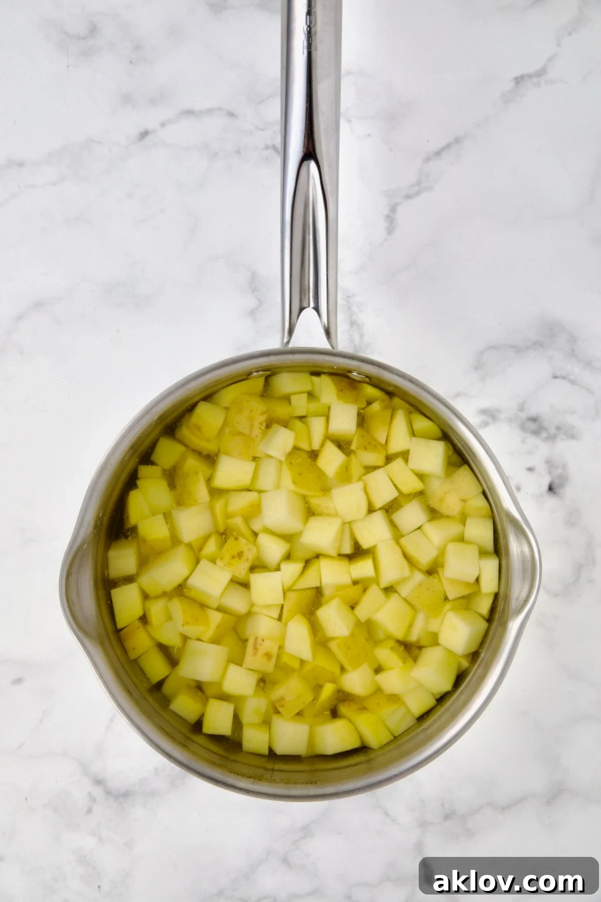 Freshly cubed Yukon Gold potatoes submerged in cold water in a stainless steel saucepan, ready for par-cooking. The water ensures even cooking as it heats.