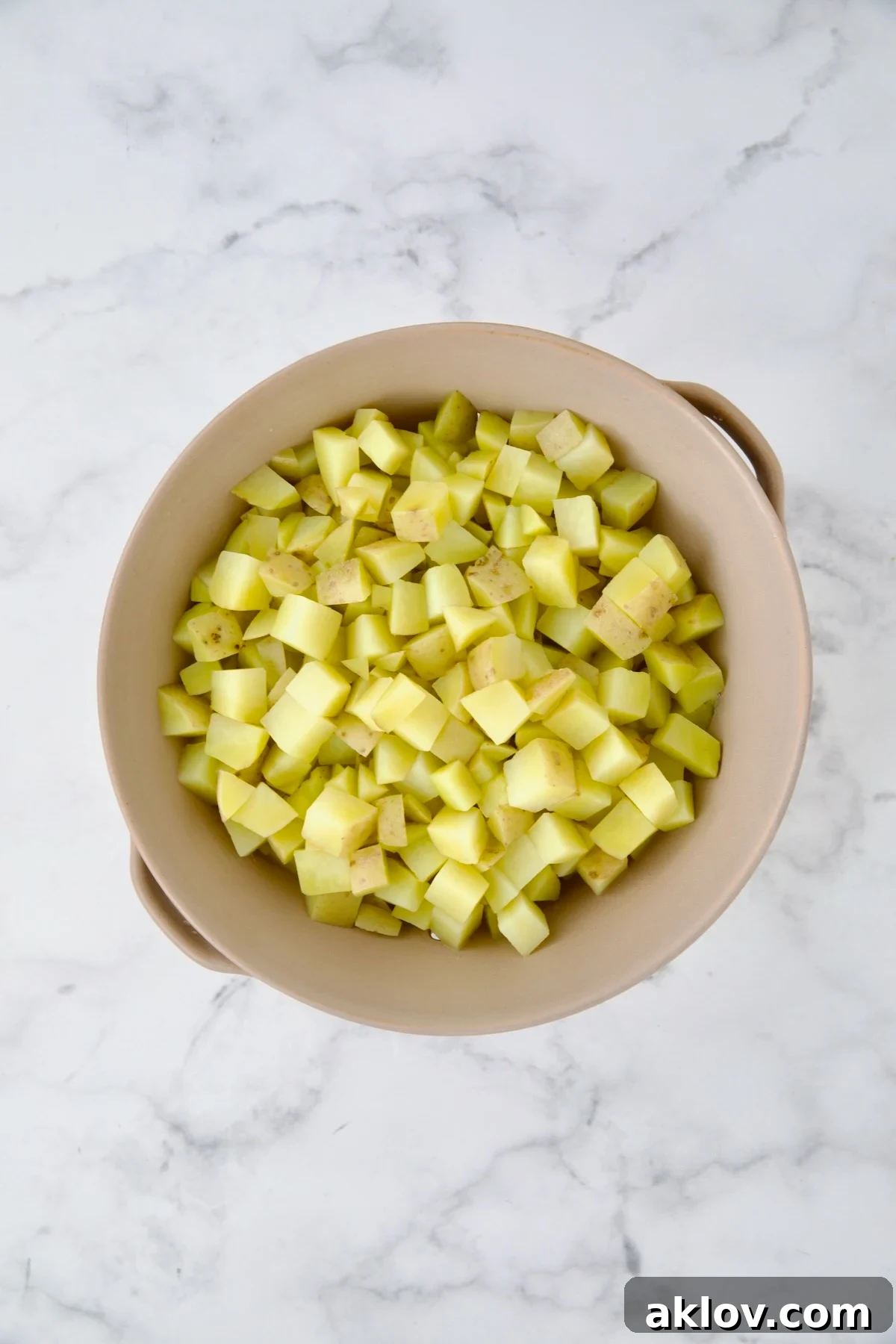 Par-cooked, cubed potatoes draining in a beige colander after being rinsed under cold water. The cooling process stops further cooking and helps them maintain their shape.