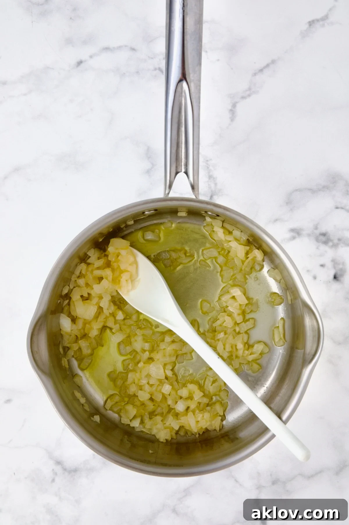 Finely chopped onions being gently sautéed in melted butter and olive oil in a stainless steel saucepan until translucent, forming the aromatic base for the cheese sauce.