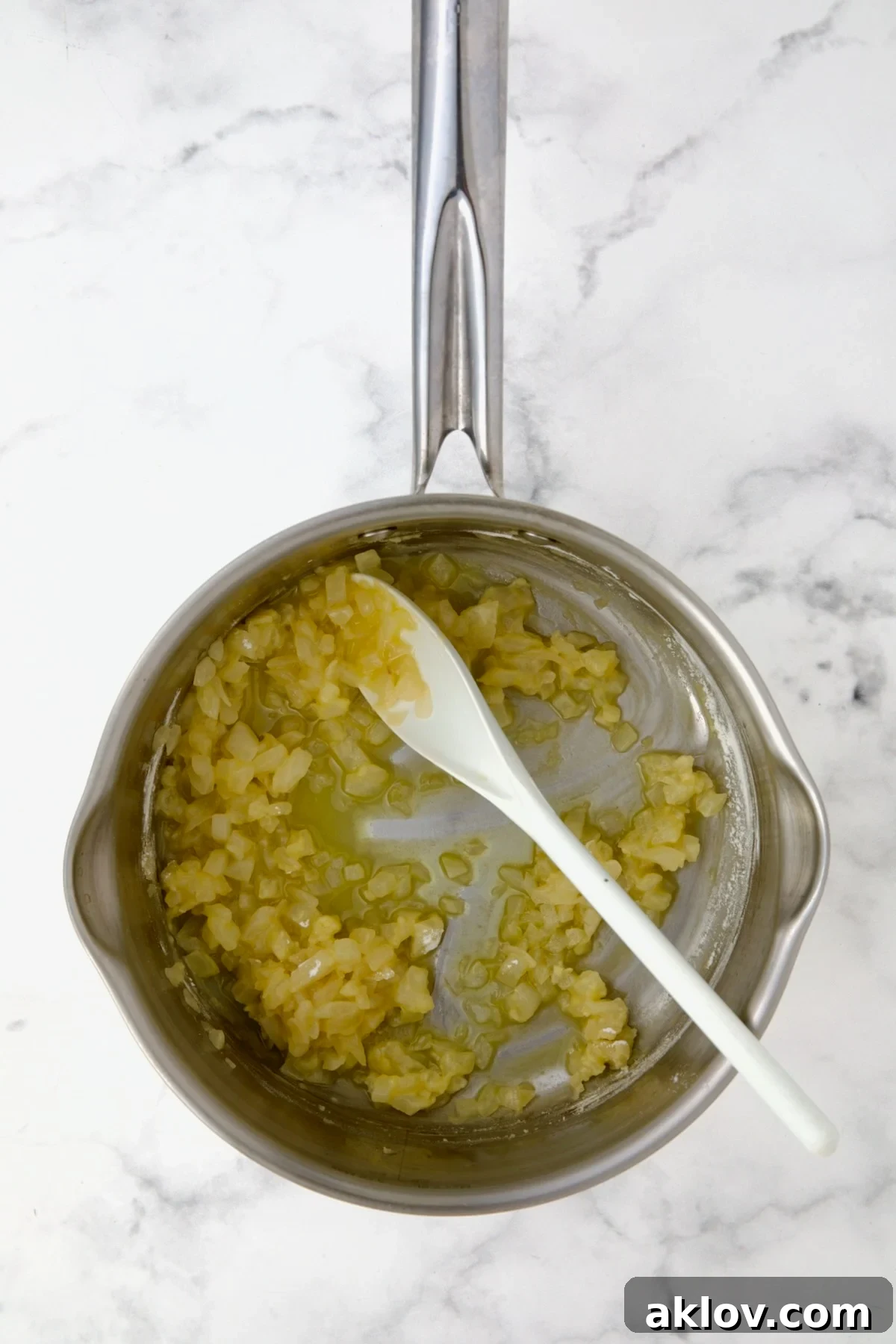 All-purpose flour added to the cooked onions in butter and oil within a stainless steel saucepan, being stirred with a white spoon to create a roux, the thickening base for the rich cheese sauce.
