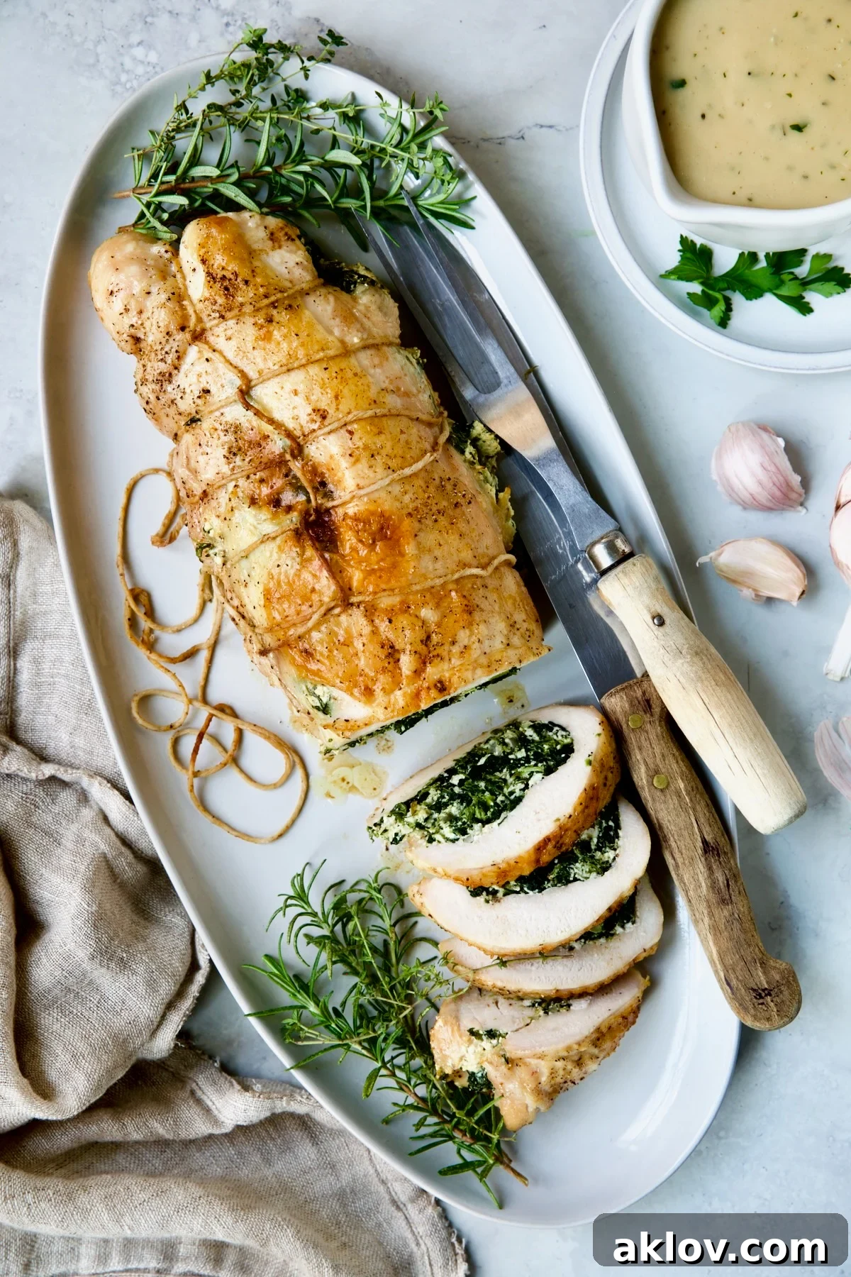 Spinach and Ricotta Stuffed Turkey Breast with Garlic - Herb Sauce on white oval platter garnished with fresh herbs, showcasing its elegant presentation.