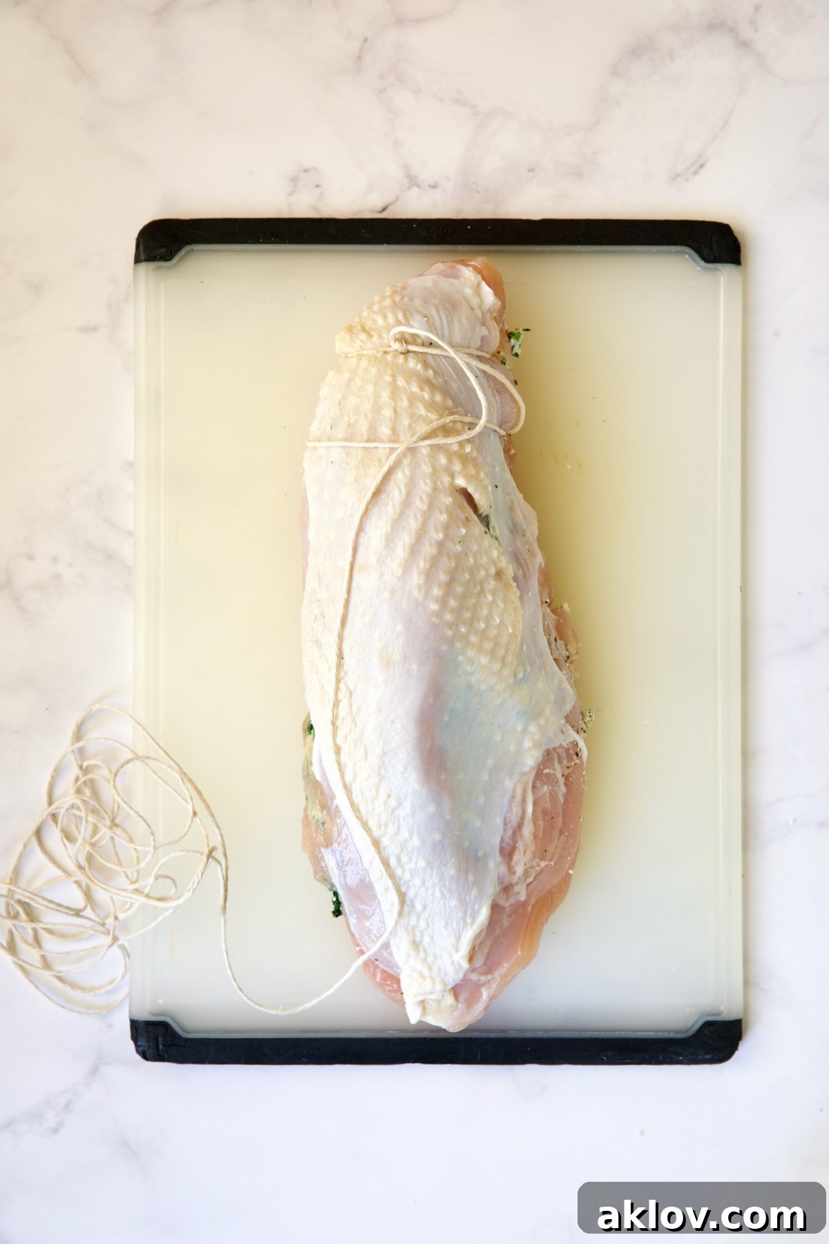 The process of tying the stuffed turkey breast with butcher's twine on a white plastic cutting board.