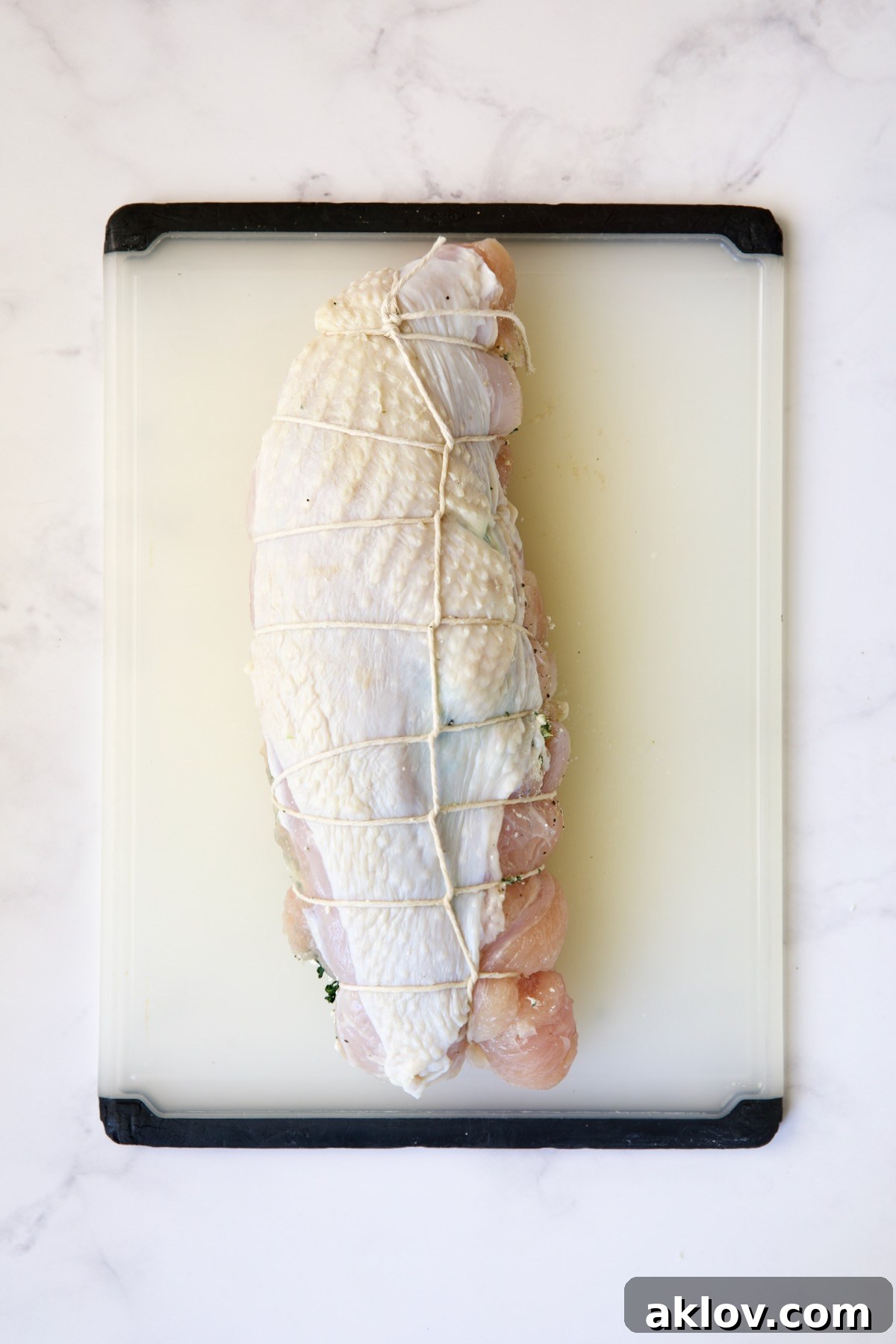 A fully tied, uncooked stuffed turkey breast ready for roasting, on a white plastic cutting board.