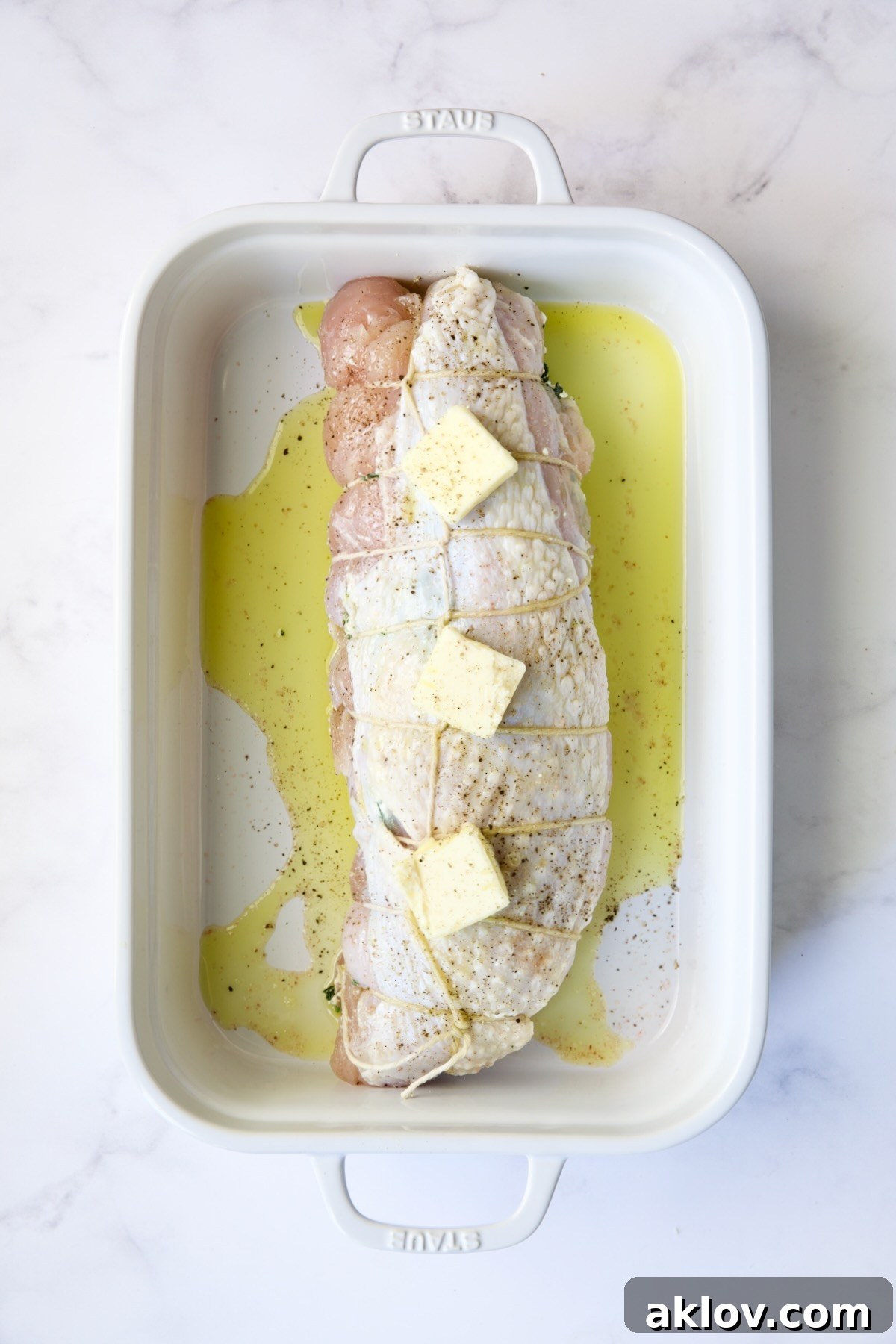 Uncooked stuffed turkey breast, generously drizzled with olive oil and topped with pats of butter, ready for the oven.