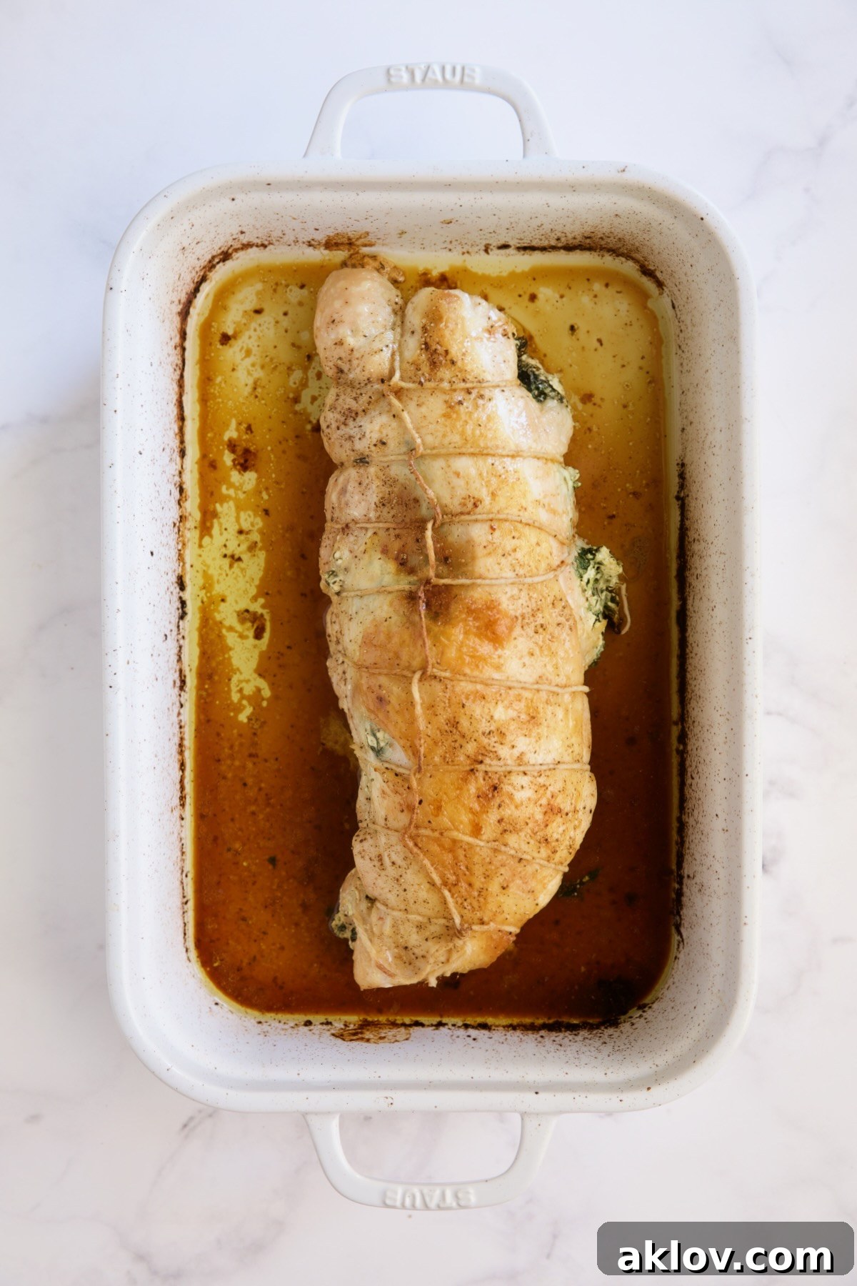 A perfectly roasted stuffed turkey breast, golden brown and resting in a white roasting pan after cooking.