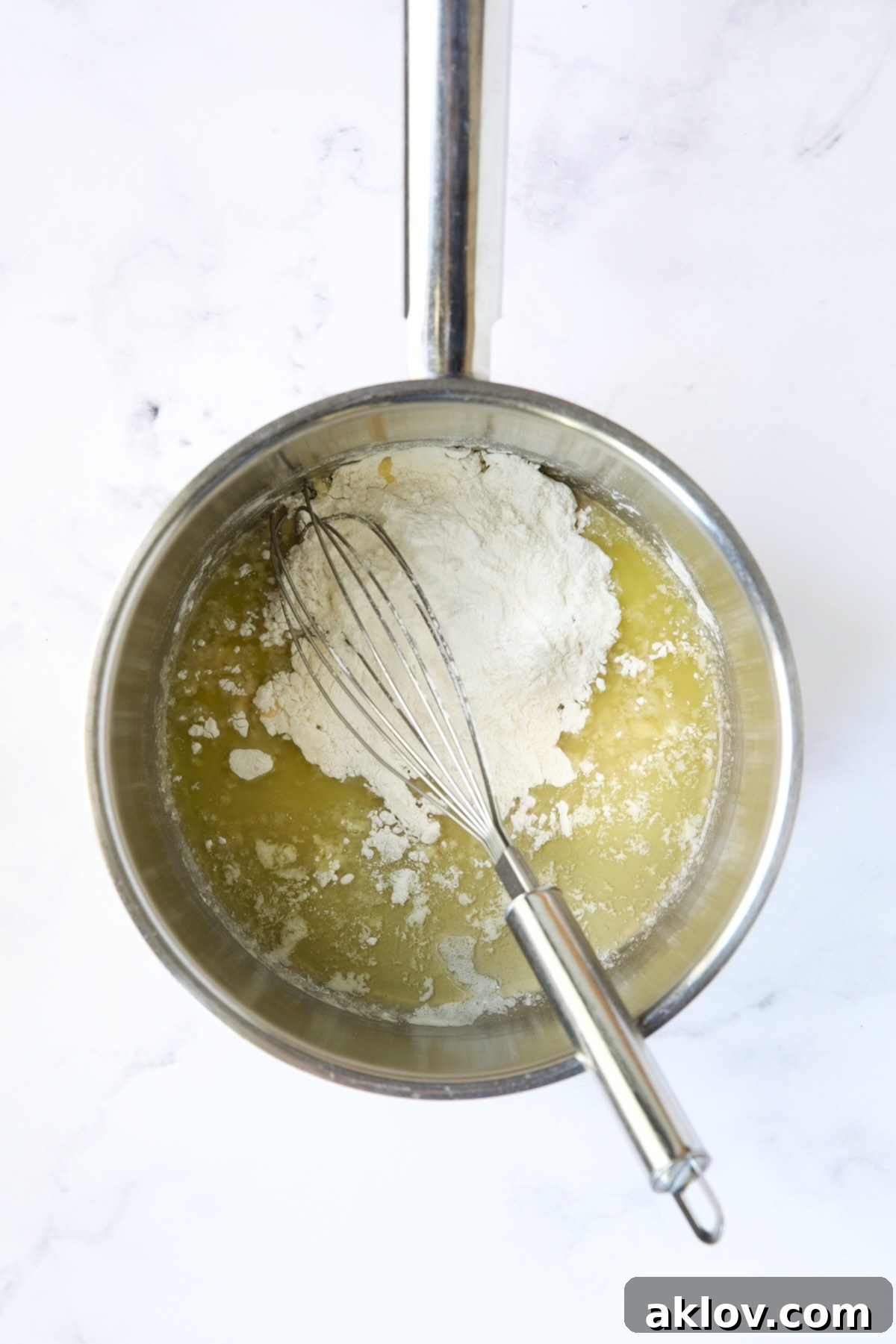 All-purpose flour being added to melted butter in a stainless steel saucepan with a wire whisk.