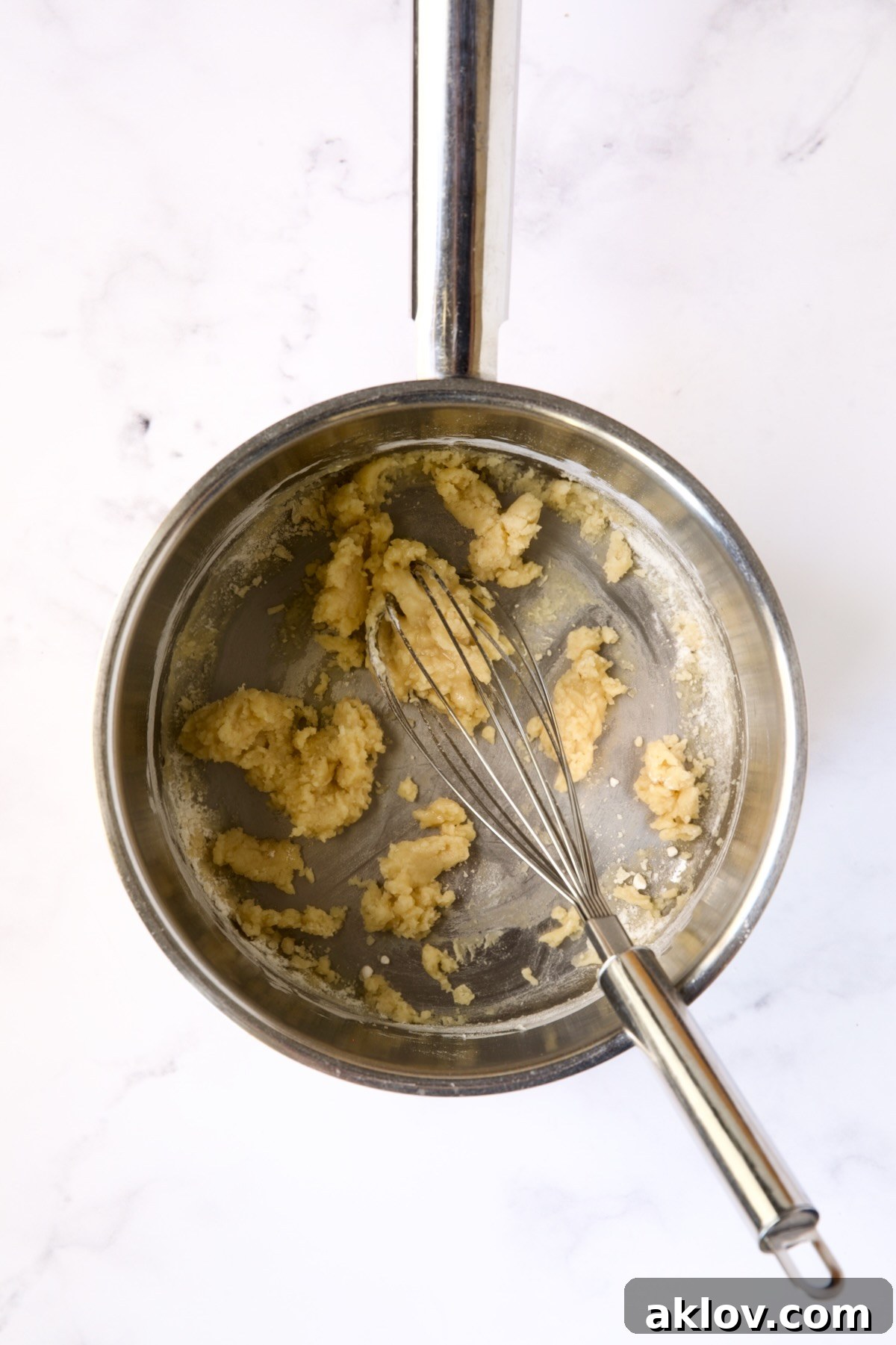 A wire whisk stirring the flour and butter mixture (roux) in a stainless steel saucepan.