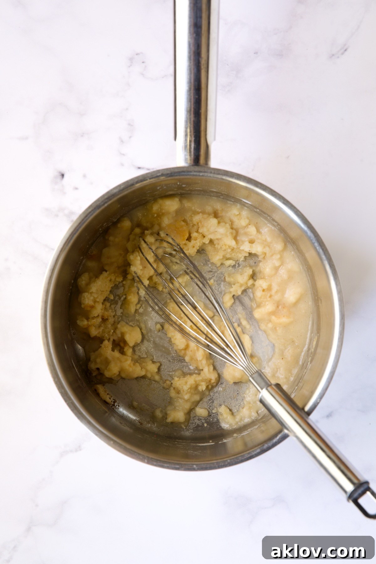 A whisk stirring dry white wine into the flour and butter mixture in a stainless steel saucepan.