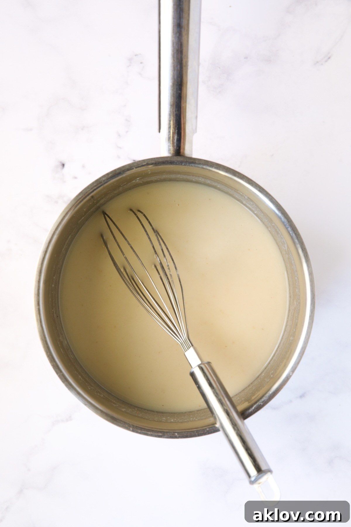 Chicken broth being added to the sauce in a stainless steel saucepan, creating a smoother consistency.
