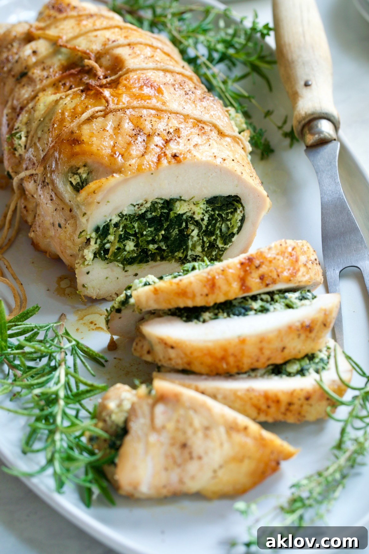 A perfectly sliced Spinach and Ricotta Stuffed Turkey Breast with Garlic - Herb Sauce on a white platter, ready for serving.
