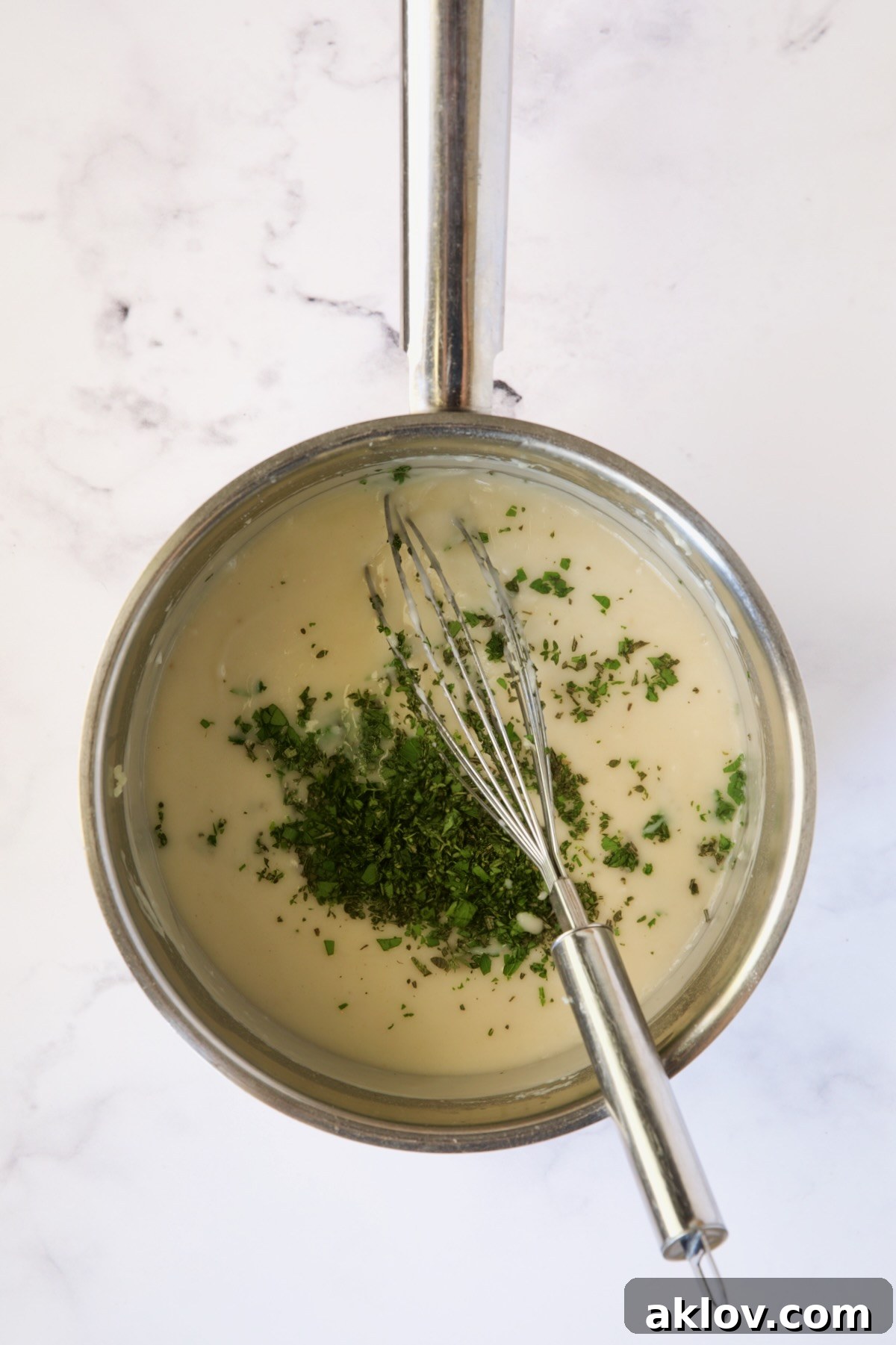 Fresh herbs, including parsley, rosemary, and thyme, added to the simmering sauce in a stainless steel saucepan.
