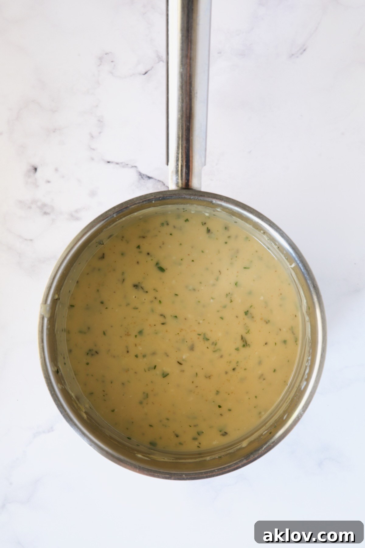The finished, perfectly thickened and flavorful garlic herb sauce in a stainless steel saucepan, ready to serve.